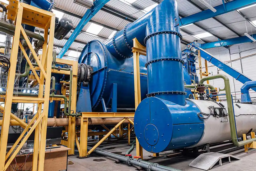 Large blue industrial processing unit connected to multiple pipes and ducts inside a factory setting.